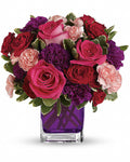 Colorful flower arrangement with red, pink, and purple flowers in a clear vase