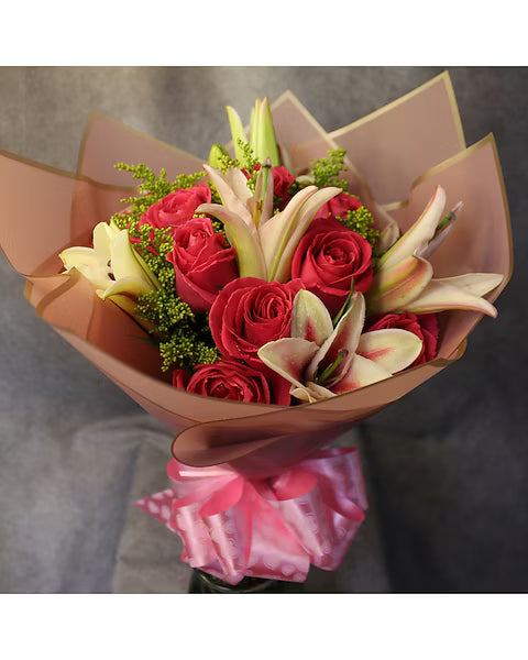 Bouquet of red roses and white lilies wrapped in brown paper with a pink ribbon on a gray background