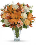 Bouquet of flowers with orange lilies, white and pink roses, and green leaves in a clear vase 