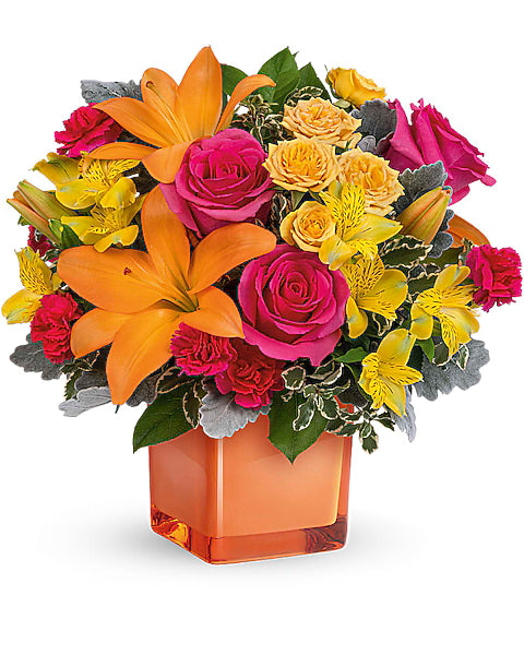 Colorful flower arrangement with orange lilies and pink roses in an orange cube vase